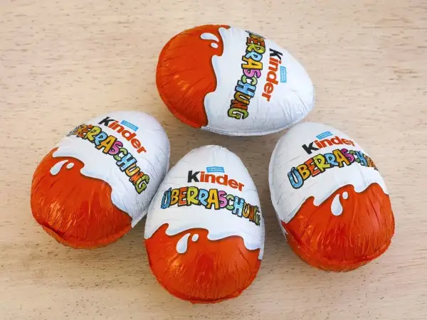 Cztery jajka Kinder Niespodzianka na drewnianym tle.